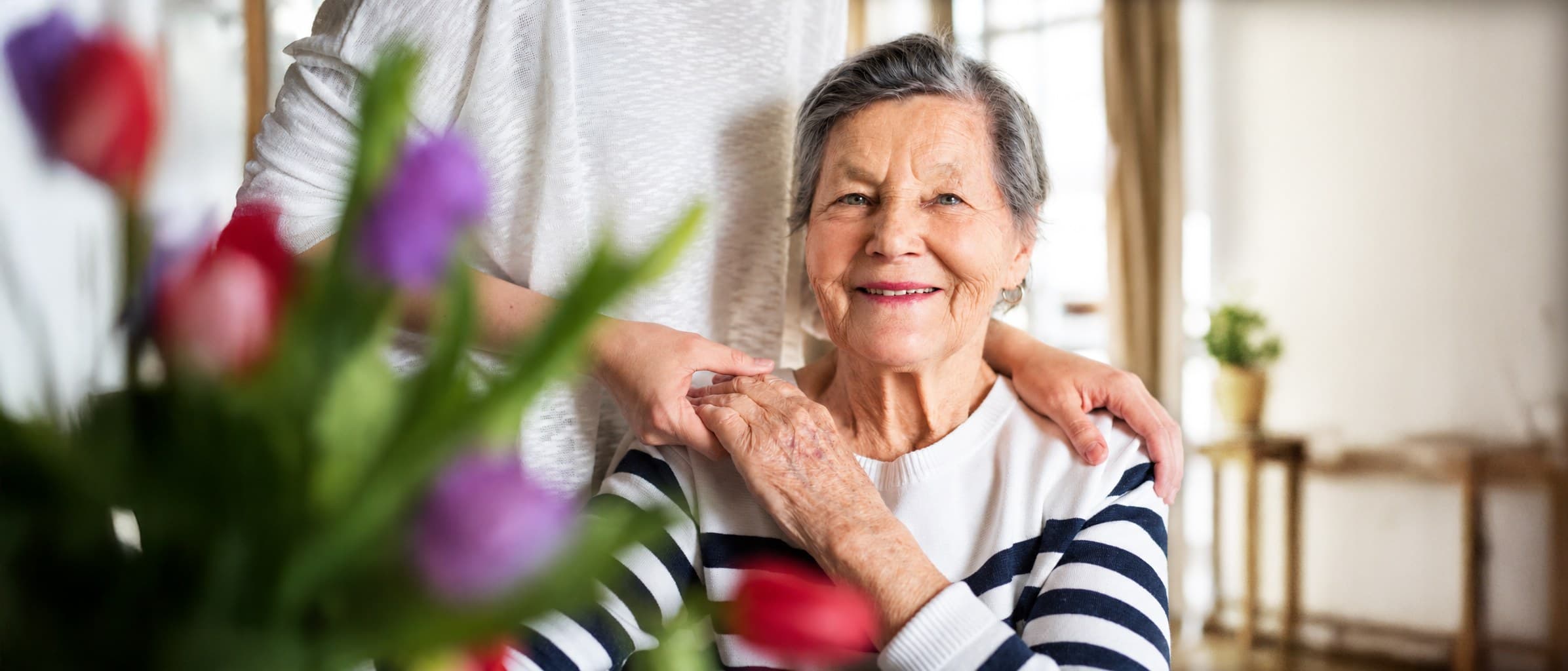 Eine lächelnde Seniorin, eine helfende Hand liegt auf ihrer Schulter